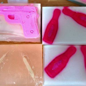 On the left is a pink Shea butter soap gun, under the gun is a clear glow bullet